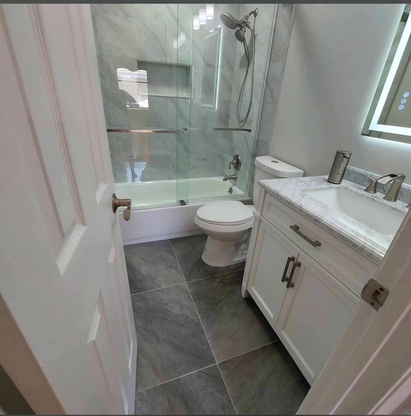 Modern bathroom with marble walls, white shaker vanity and frameless glass shower